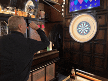 a man playing a game of darts with a bottle of budweiser in the background