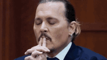 a man with a ponytail and a mustache holds his finger to his mouth