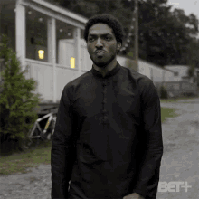 a man in a black shirt is standing in front of a white house with a bet + logo in the corner .