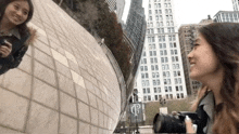 a woman taking a picture of another woman with a camera in front of a building with the letter p on it