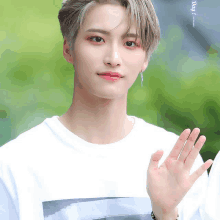 a young man wearing a white t-shirt with a picture on it waving his hand