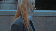 a woman with long blonde hair is smoking a cigarette in front of a building .