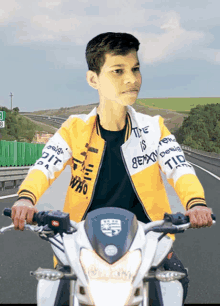 a boy is riding a motorcycle on a highway wearing a yellow jacket that says " the is " on it