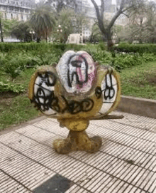 a statue with graffiti on it is sitting on a tiled sidewalk in a park .