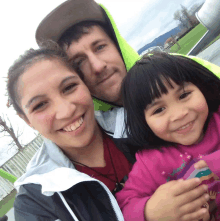 a man and a woman are posing for a picture with a little girl wearing a pink shirt that says " a friend "