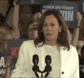 a woman is giving a speech in front of a crowd while holding a sign that says when we fight .