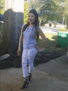 a woman in a blue shirt and white pants is standing on a sidewalk .