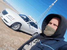 a man wearing a face mask stands in front of a chrysler car