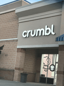 the outside of a crumbl store with a trash can in front of it