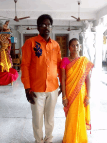 a man in an orange shirt stands next to a woman in a yellow saree