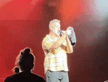 a man in a plaid shirt sings into a microphone while a woman watches