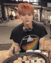 a man wearing a dark side of the moon t-shirt sits at a table with food