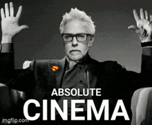 a man in a suit and glasses is sitting in a chair with his arms outstretched and the words absolute cinema behind him