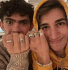 two young men are posing for a picture with their hands covered in rings .