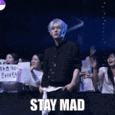 a man in a black jacket stands in front of a crowd with a sign that says stay mad