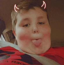 a boy with horns on his head is sticking his tongue out while sitting in a car .