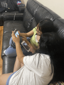 two girls sitting on a couch looking at their cell phones