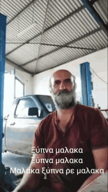 a man with a beard is sitting in front of a truck in a garage with a caption in greek