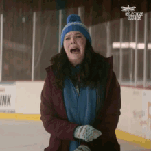 a woman wearing a blue hat and gloves is crying on a ice rink with gilmore glue in the background