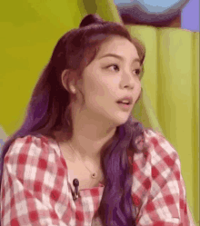 a close up of a woman with purple hair wearing a plaid shirt and a necklace .