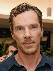 a close up of a man 's face with curly hair wearing a blue shirt .