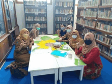 a group of women wearing face masks sit around a table in a library .