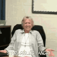 an older woman is sitting at a desk with her arms outstretched and the words stop feeling angry written above her .