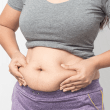 a woman in a grey shirt and purple shorts holds her stomach