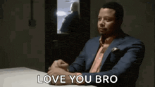 a man in a suit is sitting at a table with his hands folded and says `` love you bro '' .