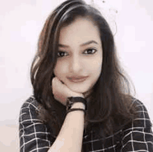 a woman in a plaid shirt is sitting with her hand on her chin and wearing a watch .