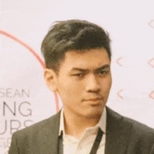 a young man wearing a suit and tie is standing in front of a white wall .