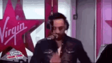 a man is singing into a microphone in front of a virgin radio sign .