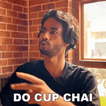 a man with a beard says do cup chai in front of a window