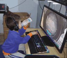 a young boy drinks from a bottle while playing a video game on a computer