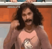 a man with long hair and a mustache is wearing a unicorn shirt and giving a thumbs up .