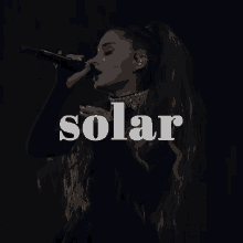 ariana grande singing into a microphone with the word solar behind her