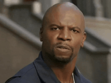 a bald man with a beard is standing in front of stairs looking at the camera .