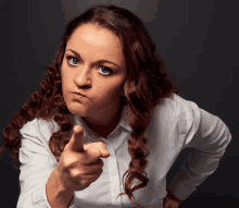 a woman with curly hair is pointing at the camera