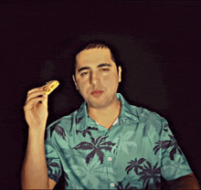 a man in a blue shirt with palm trees on it is holding a donut