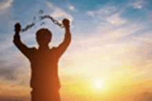 a silhouette of a man holding chains in his hands at sunset .