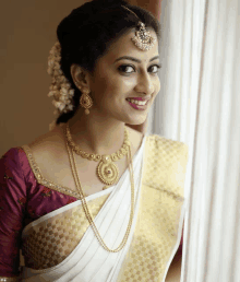 a woman wearing a white saree and gold jewelry smiles