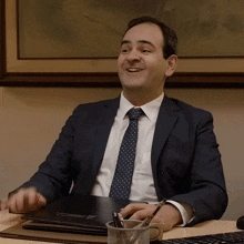 a man in a suit and tie is smiling while sitting at a desk with a folder that says ' attorney '