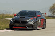 a black and red car is driving down a road next to a field .