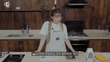 a woman in an apron stands in front of a stove in a kitchen with a carton of milk in front of her