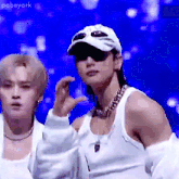 a man wearing a white hat and sunglasses is standing next to another man wearing a white tank top .
