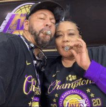 a man smoking a cigar next to a woman wearing a lakers t-shirt