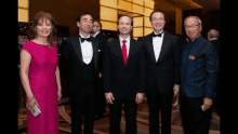 a woman in a pink dress stands next to four men in tuxedos