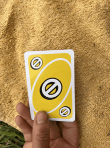 a hand is holding a yellow uno card in front of a yellow blanket