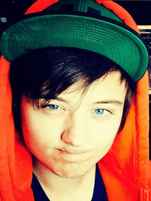 a young boy wearing an orange hoodie and a green hat makes a funny face