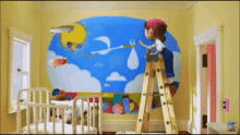 a person is standing on a ladder painting a mural on a wall in a nursery .